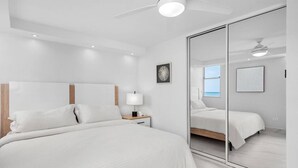 A modern bedroom with a large bed, a bedside table with a lamp, a ceiling fan, and a large mirror.