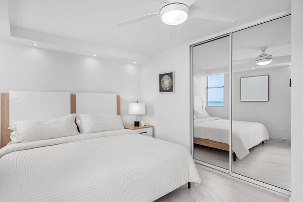 Une chambre moderne avec un grand lit, une table de chevet avec une lampe, un ventilateur de plafond et un grand miroir.