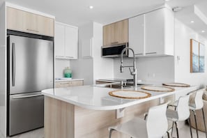 A modern kitchen with a stainless steel refrigerator, white cabinets, a central island with woven placemats, and a stainless steel faucet. - Beachfront Sanctuary Newly Renovated to Perfection with Full Power Generator (Carolina)