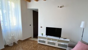 A living room with a wooden floor, a television on a white stand, a sofa with pink cushions, and a ceiling fan. - Detached house and outdoor terrace (Palermo)