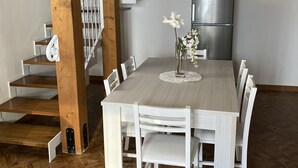 A dining area with a wooden table and white chairs, a modern clock on the wall, and a staircase with a white railing. - Detached house and outdoor terrace (Palermo)
