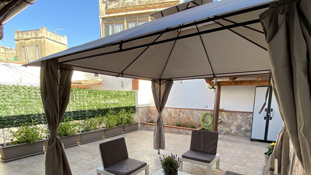 A covered outdoor seating area with a table and chairs, a potted plant, and a view of buildings in the background. - Detached house and outdoor terrace (Palermo)