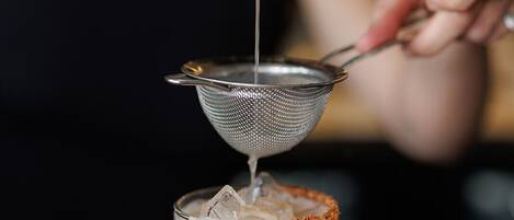 A person pouring a clear liquid into a glass with ice and a rim of orange spice.