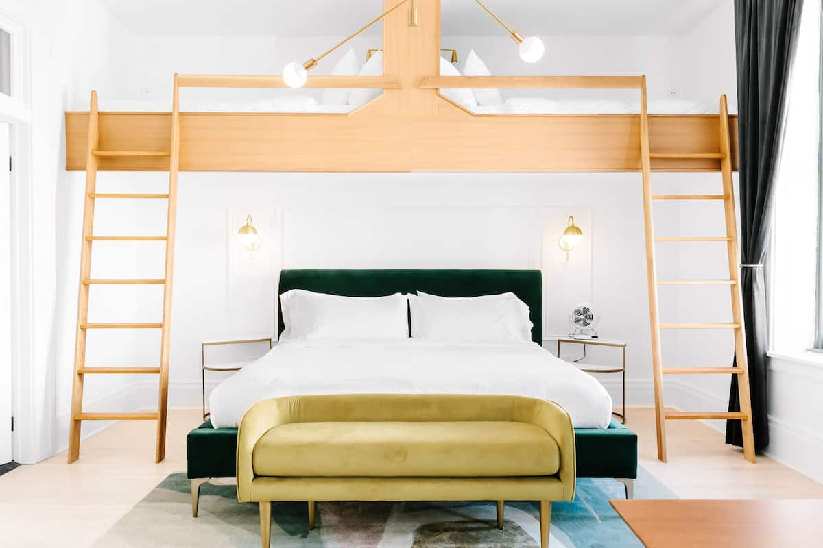 A modern bedroom with a bunk bed, wooden ladder, bedside tables, and a green headboard.