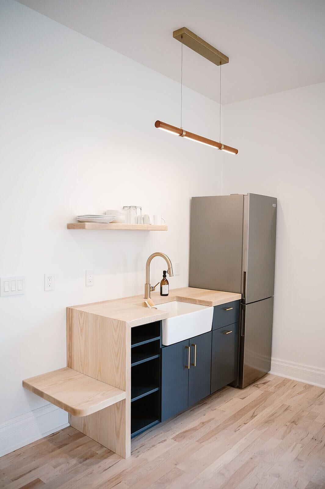 A compact kitchen with a built-in sink, a stainless steel refrigerator, and a wooden countertop.