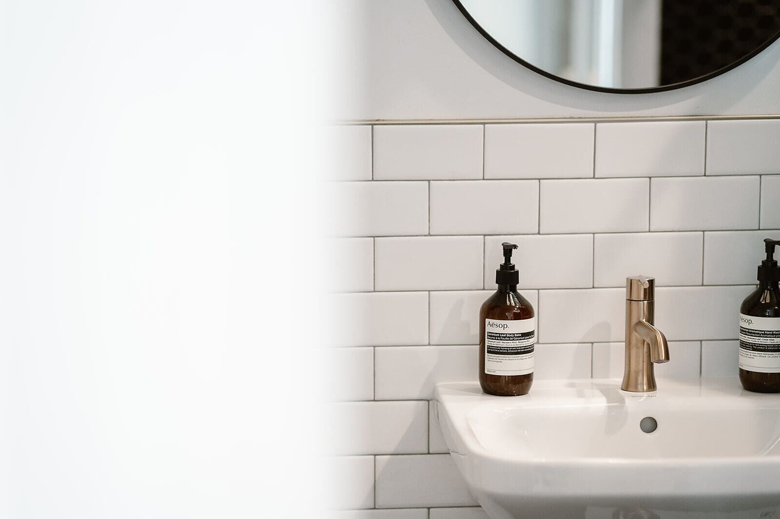 A bathroom with white tiled walls, a white sink, and two bottles of Aesop hand wash soap.