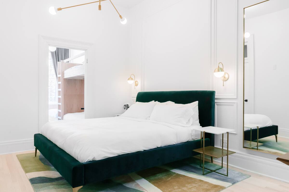 A modern bedroom with a green upholstered bed, a small bedside table, and a large mirror.