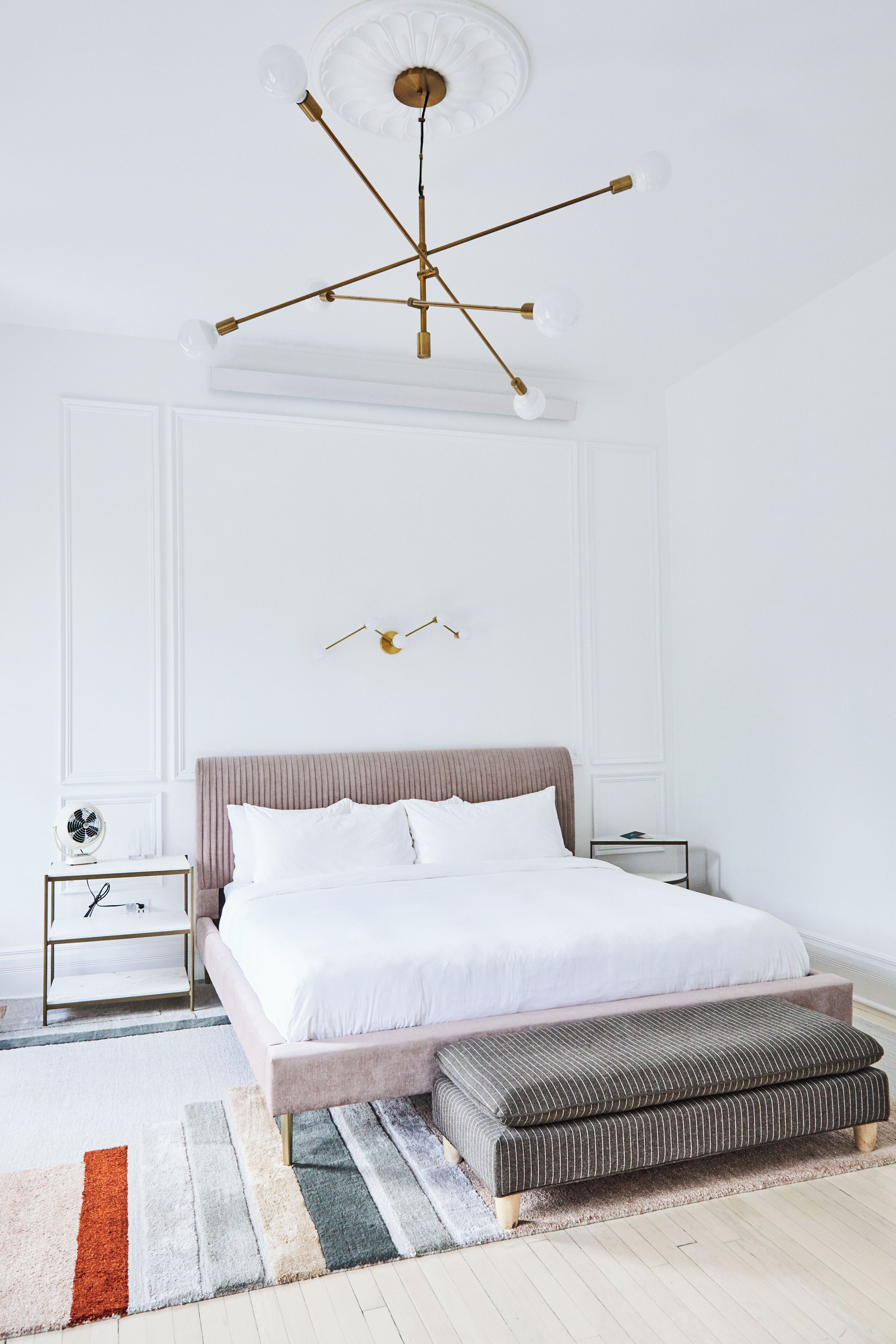 A bedroom with a bed, bedside tables, a bench, a ceiling light fixture, and a wall-mounted light.