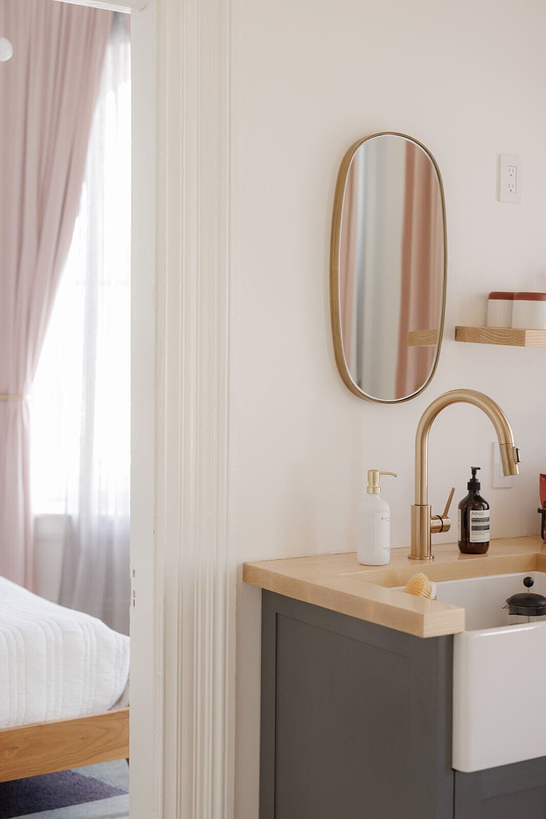 A modern bathroom with a wooden vanity, a large mirror, a gold faucet, and a bottle of shampoo.