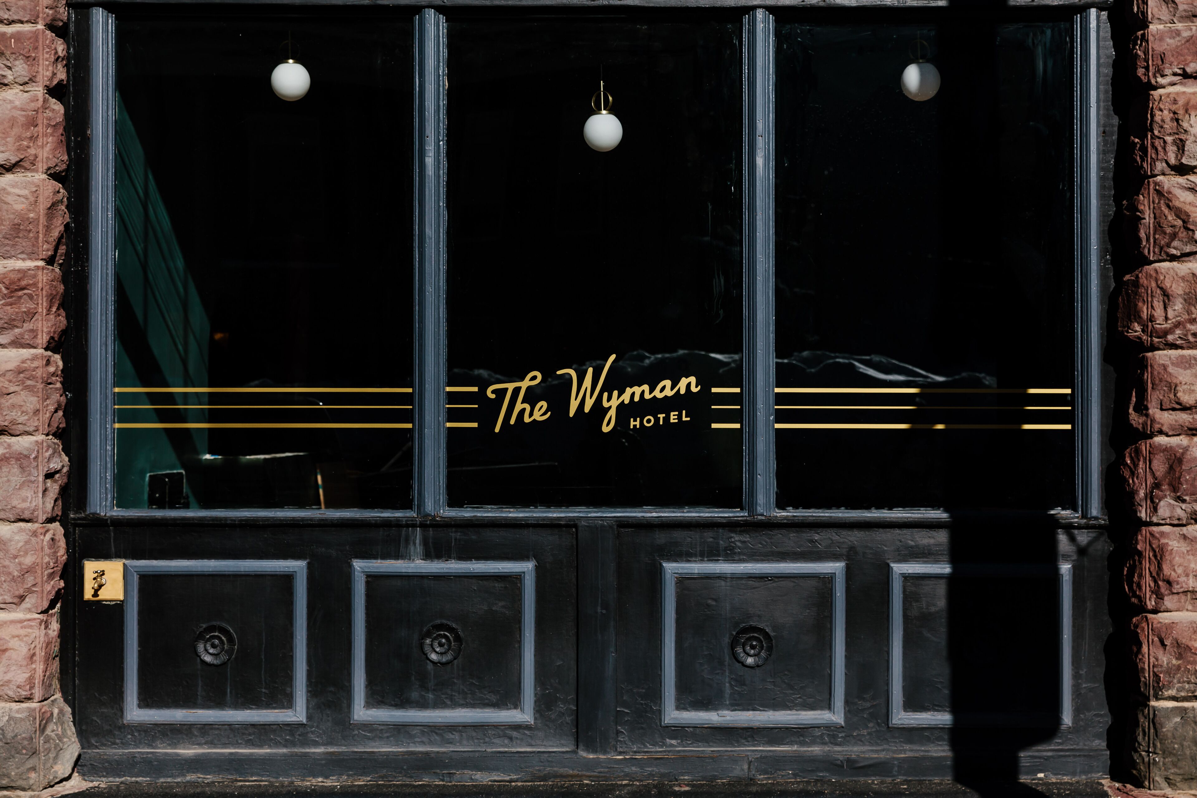 A black-framed window with the text "The Wyman Hotel" in gold lettering, set in a brick building.
