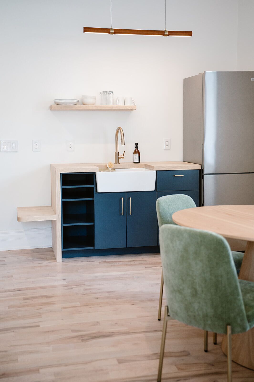 A modern kitchen with a built-in sink, a stainless steel refrigerator, and a wooden dining table with green chairs.