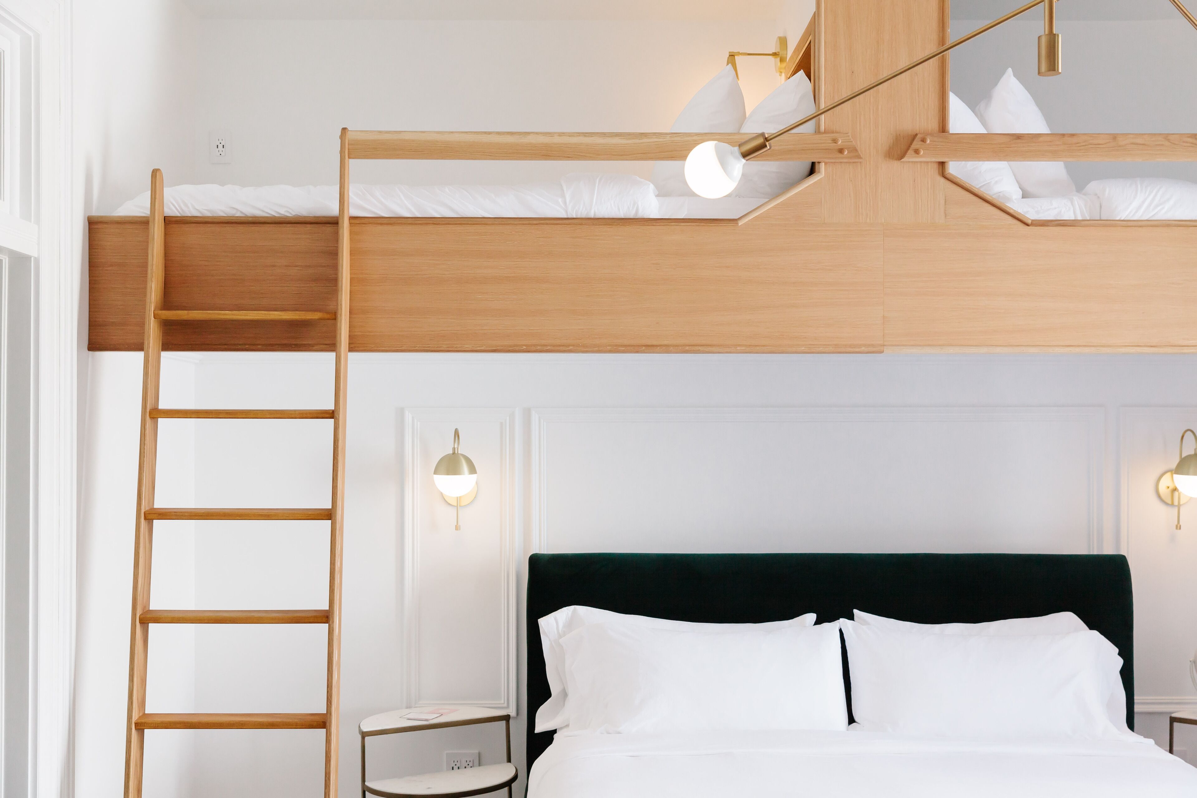 A bunk bed with a wooden ladder, two bedside tables with lamps, and a dark green headboard.