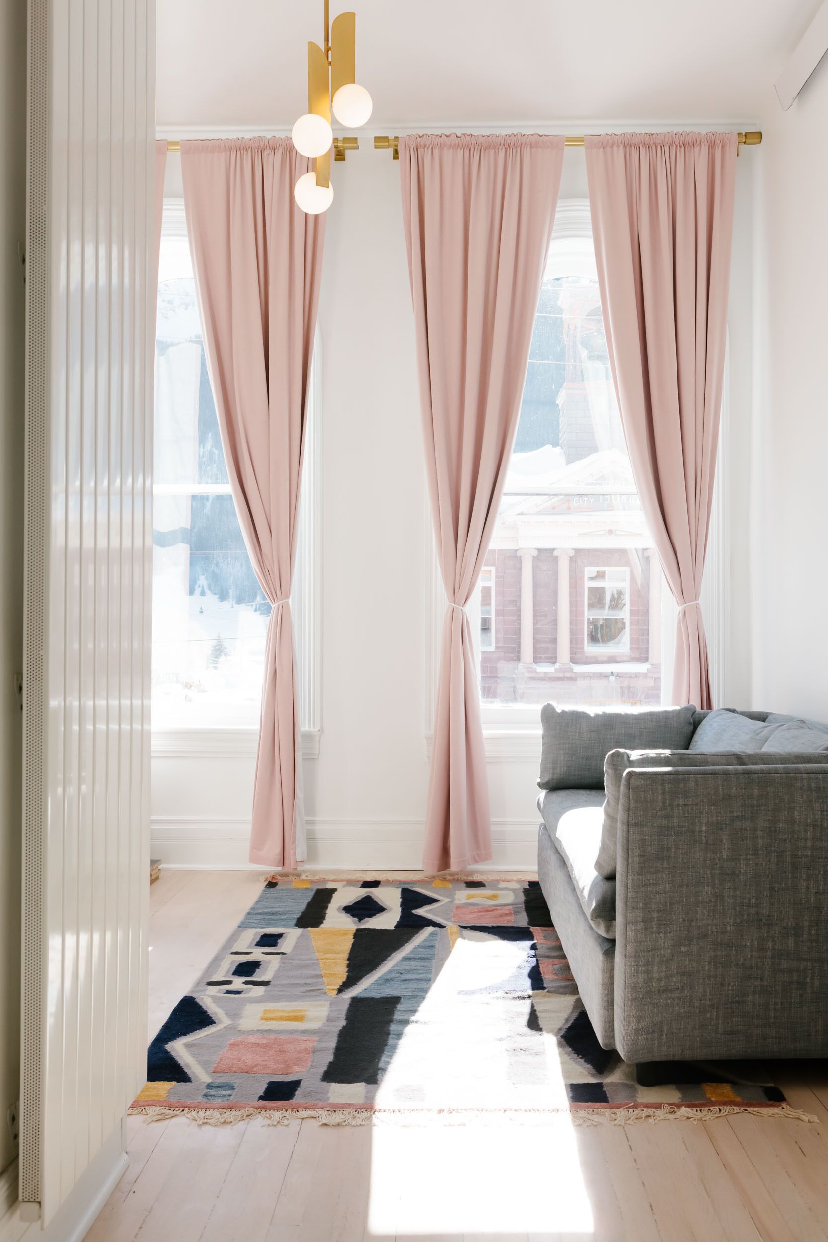 Un salon moderne avec un canapé gris, un tapis à motifs et des rideaux roses.