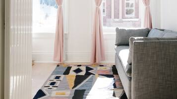 Un salon moderne avec un canapé gris, un tapis à motifs et des rideaux roses.