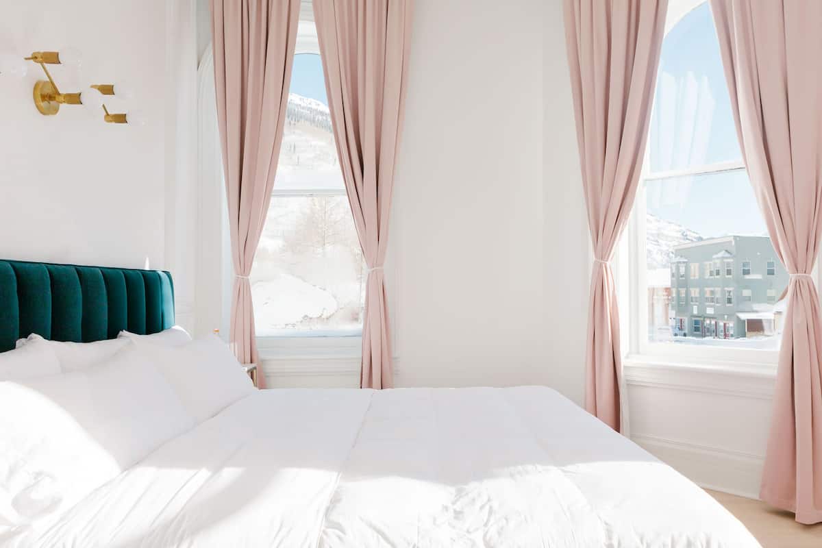A bedroom with a large bed, a teal headboard, and pink curtains.