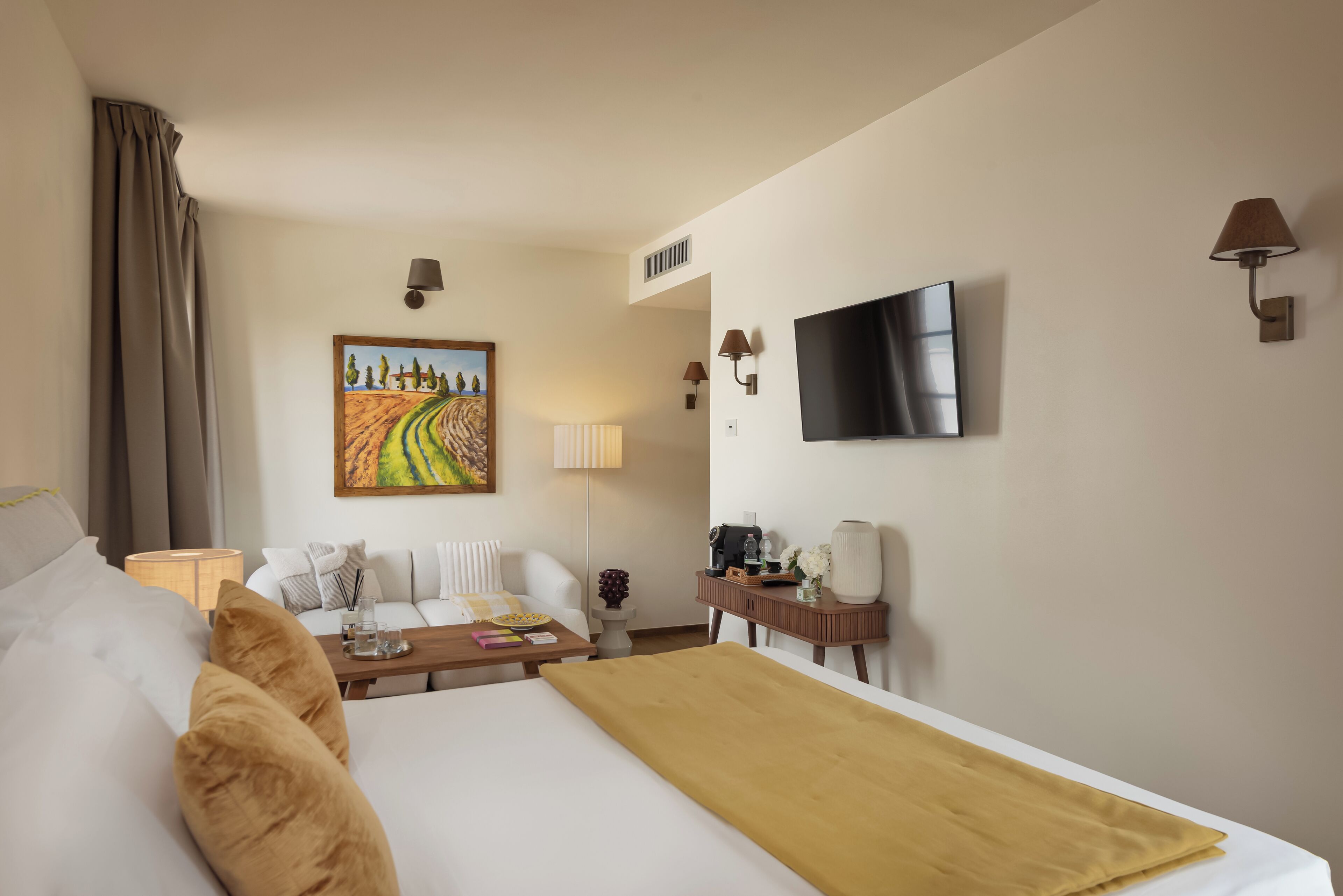 Una habitación de hotel con cama, sofá, escritorio con lámpara, televisor y un cuadro en la pared.