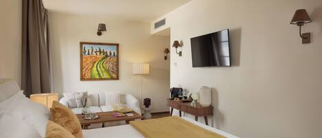 Una habitación de hotel con cama, sofá, escritorio con lámpara, televisor y un cuadro en la pared.