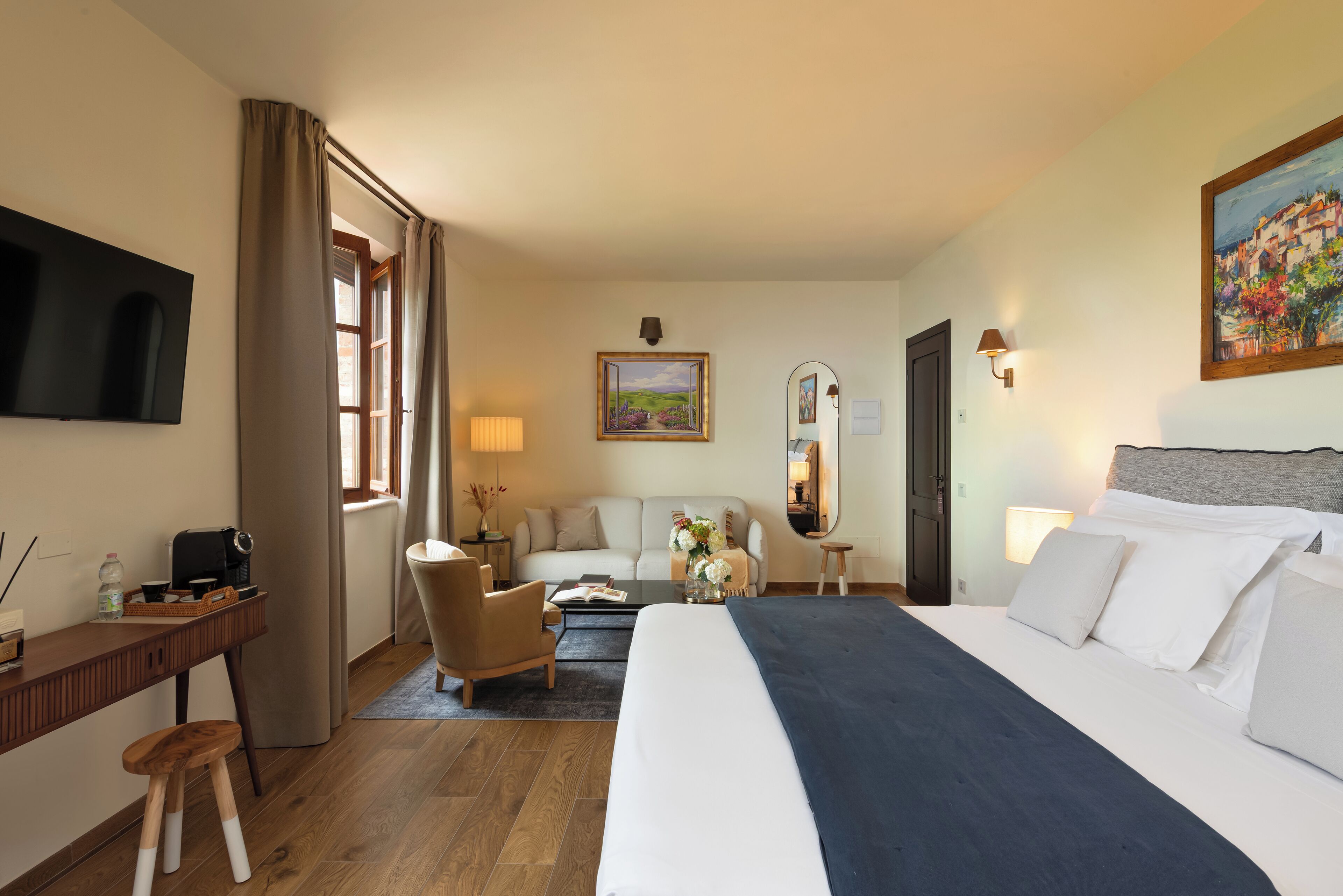 Une chambre d’hôtel avec un lit, un bureau, une chaise, un canapé, une télévision et un tableau au mur.