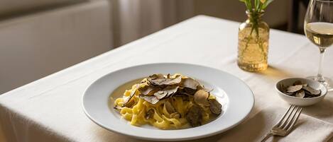 A plate of pasta with mushrooms, a glass of white wine, and a vase with yellow flowers on a table.
