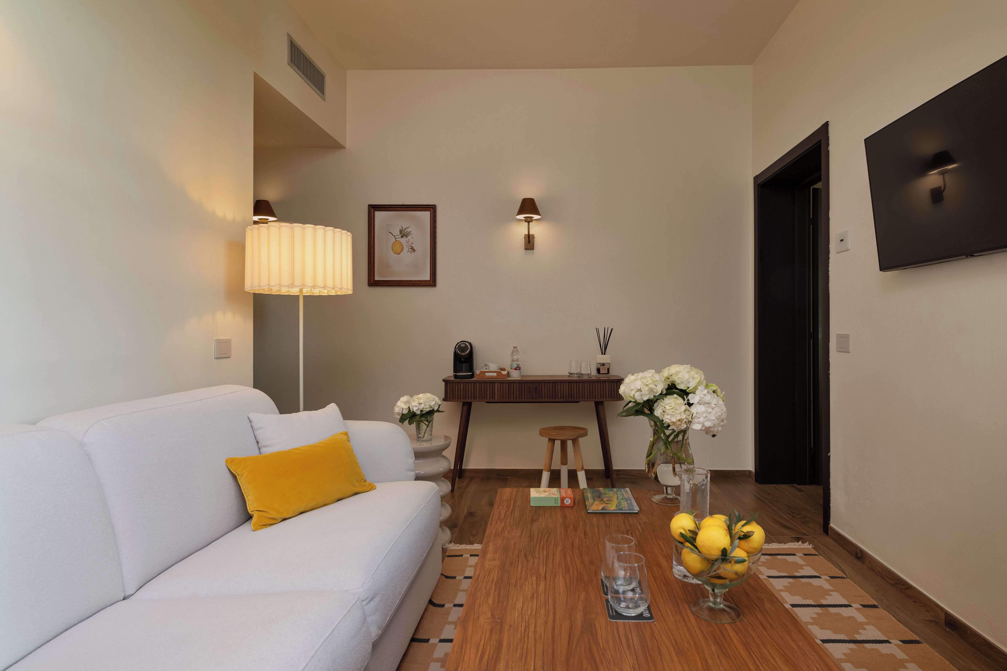A modern living room with a white sofa, a wooden coffee table, and a small side table with a lamp and decorative items.