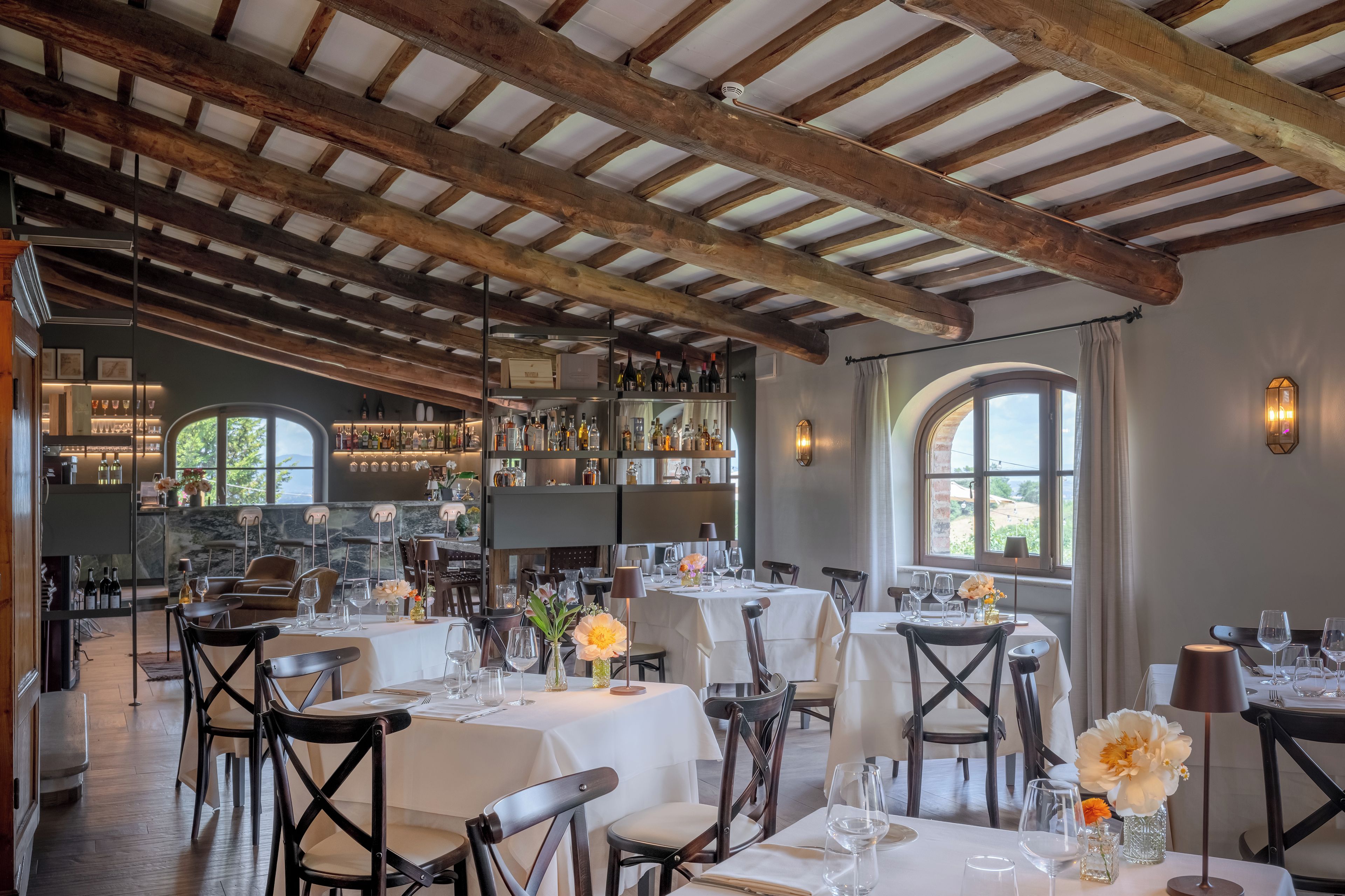 A restaurant with wooden beams, tables set for dining, and a bar area with bottles.