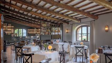 Un restaurante con vigas de madera, mesas dispuestas para comer y una zona de bar con botellas.