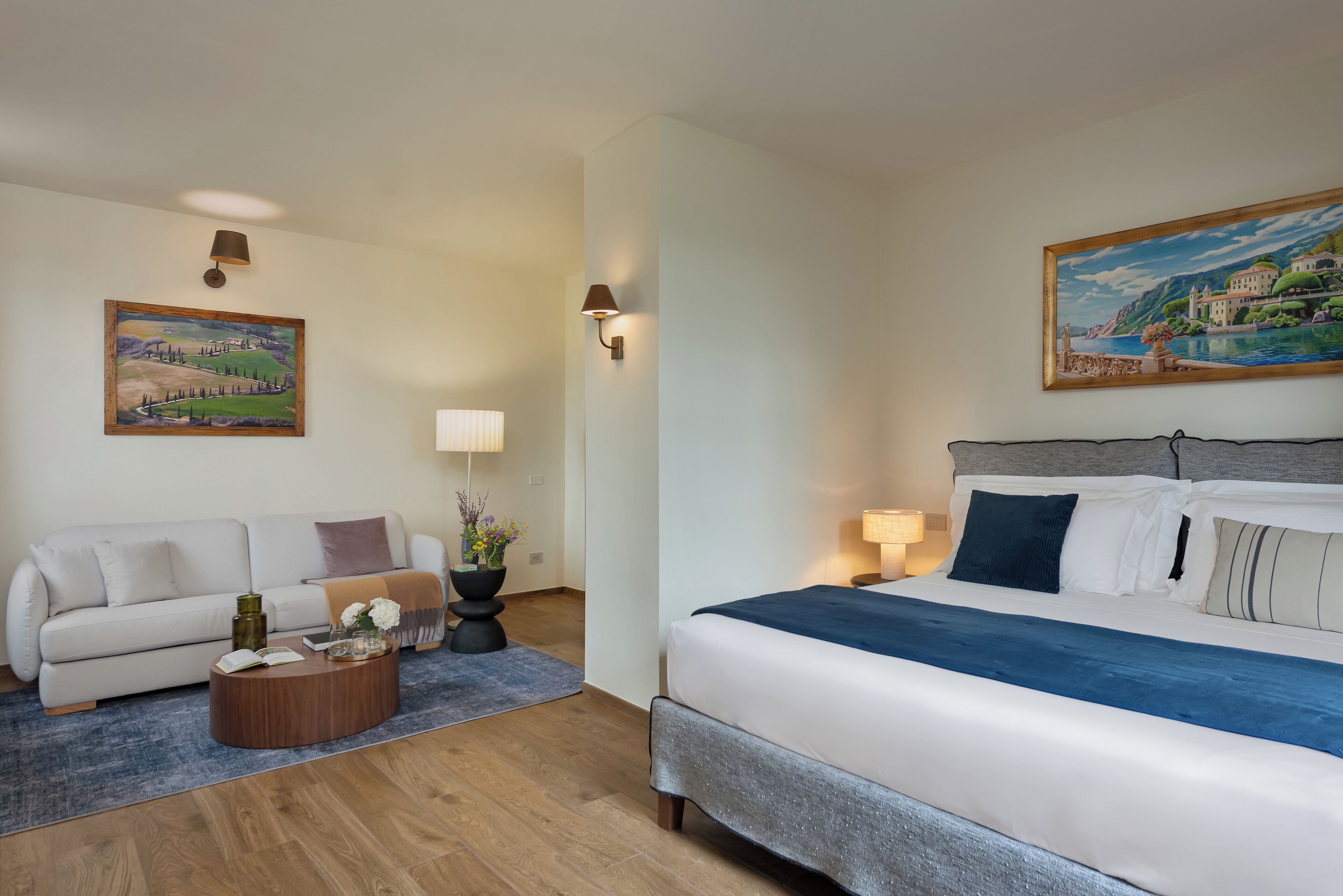 Una habitación de hotel con una cama, un sofá, una mesa de centro y dos cuadros en las paredes.