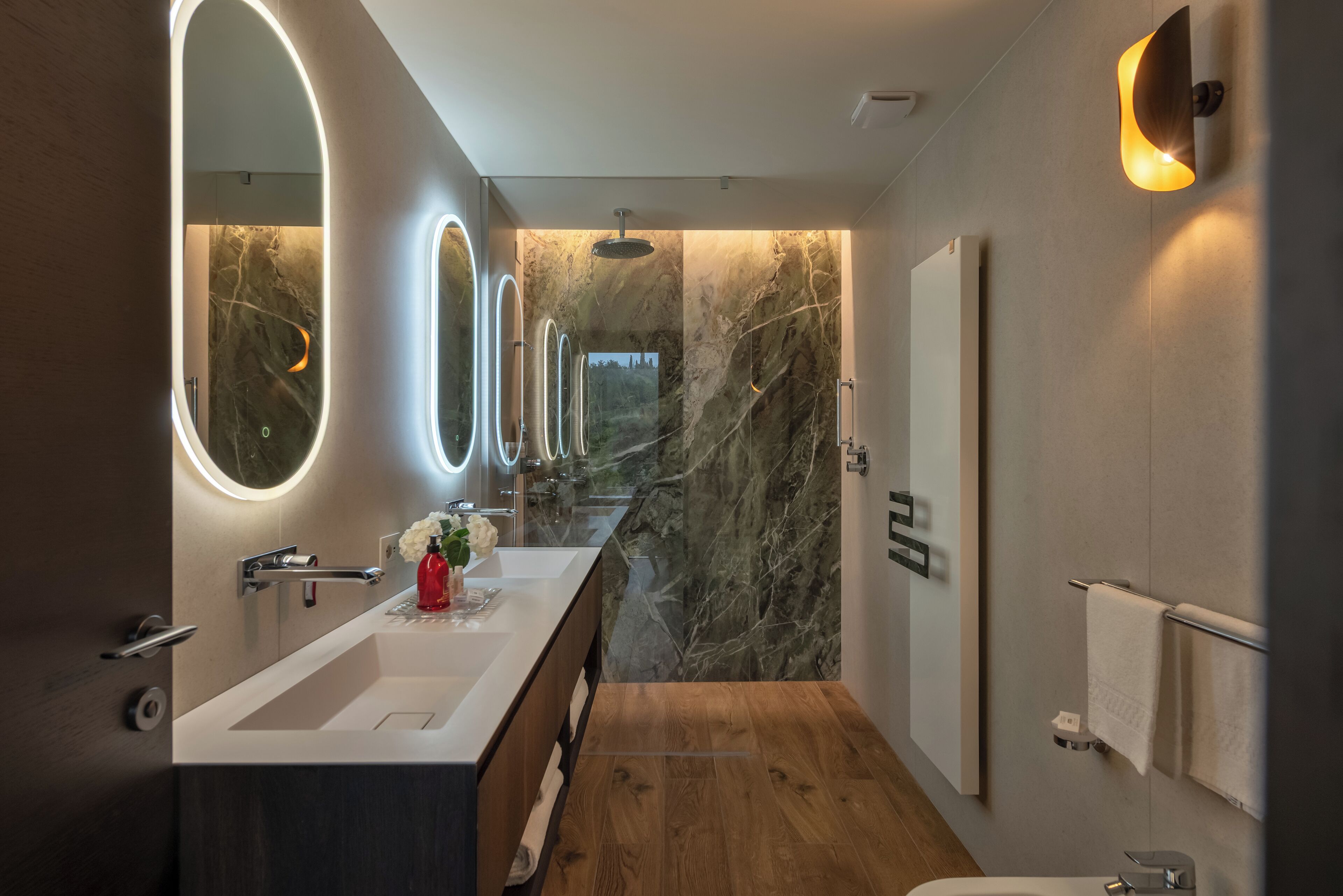 A modern bathroom with a large mirror, a wooden floor, and a marble wall.