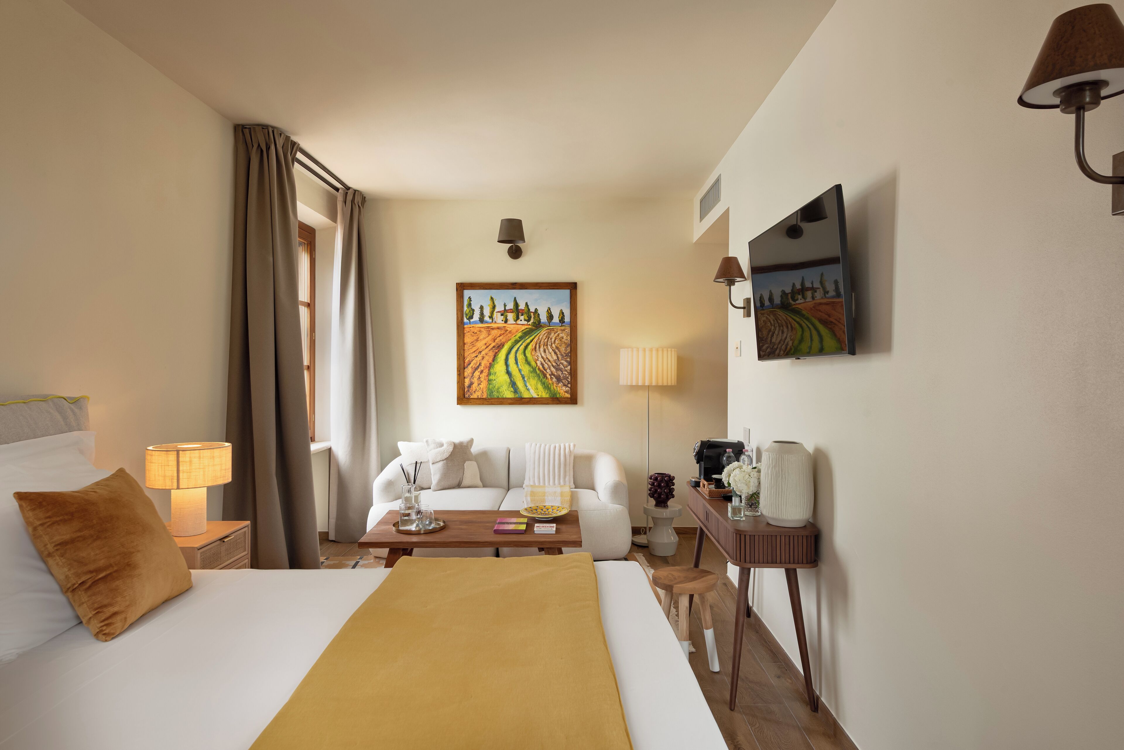 Ein Hotelzimmer mit einem Bett, einem Schreibtisch, einem Sessel, einer Lampe, einem Bild und einem Fenster mit Vorhängen.