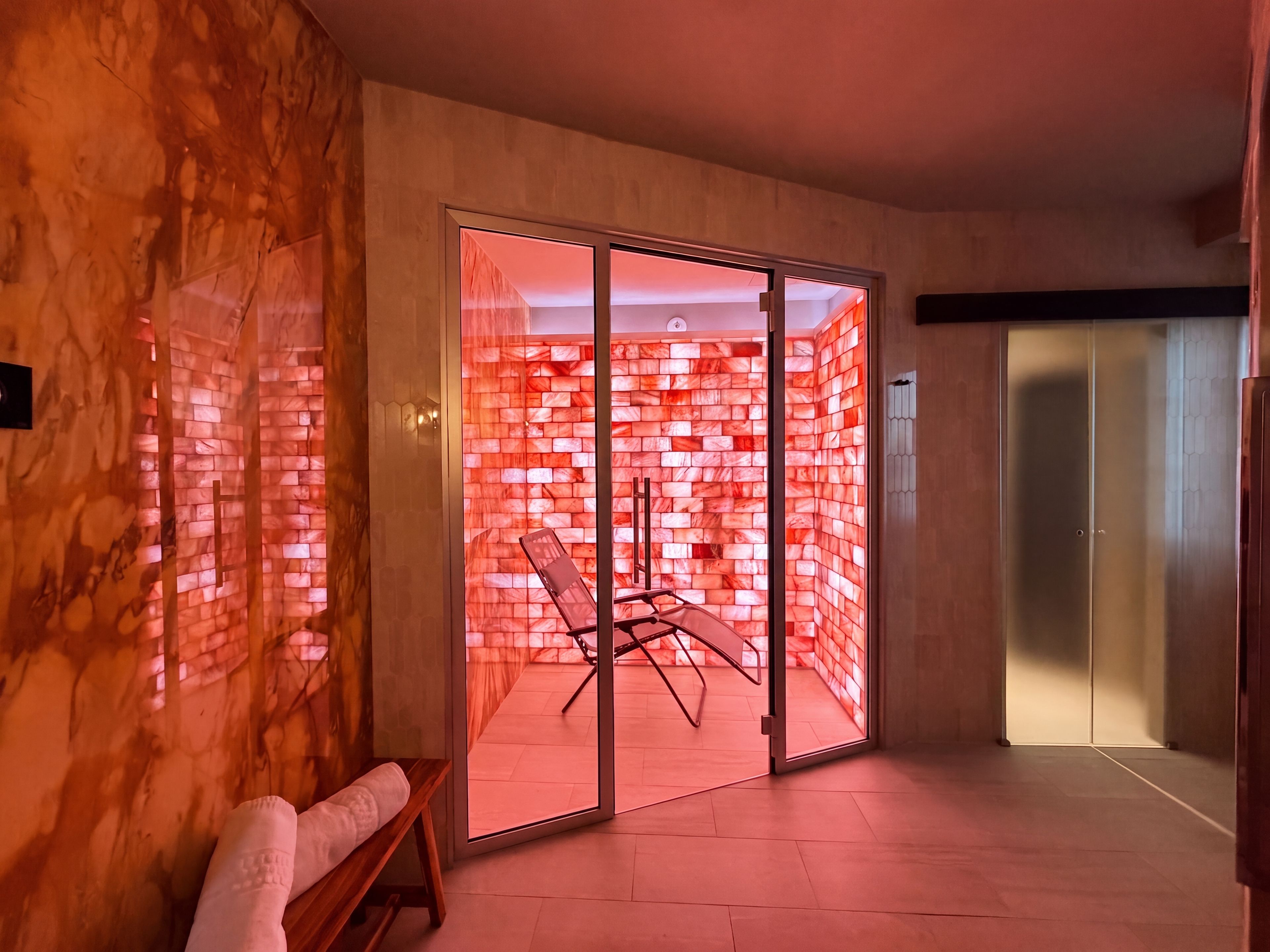Un interno moderno con una porta scorrevole in vetro che dà su un ambiente con parete in mattoni rossi e una sedia.
