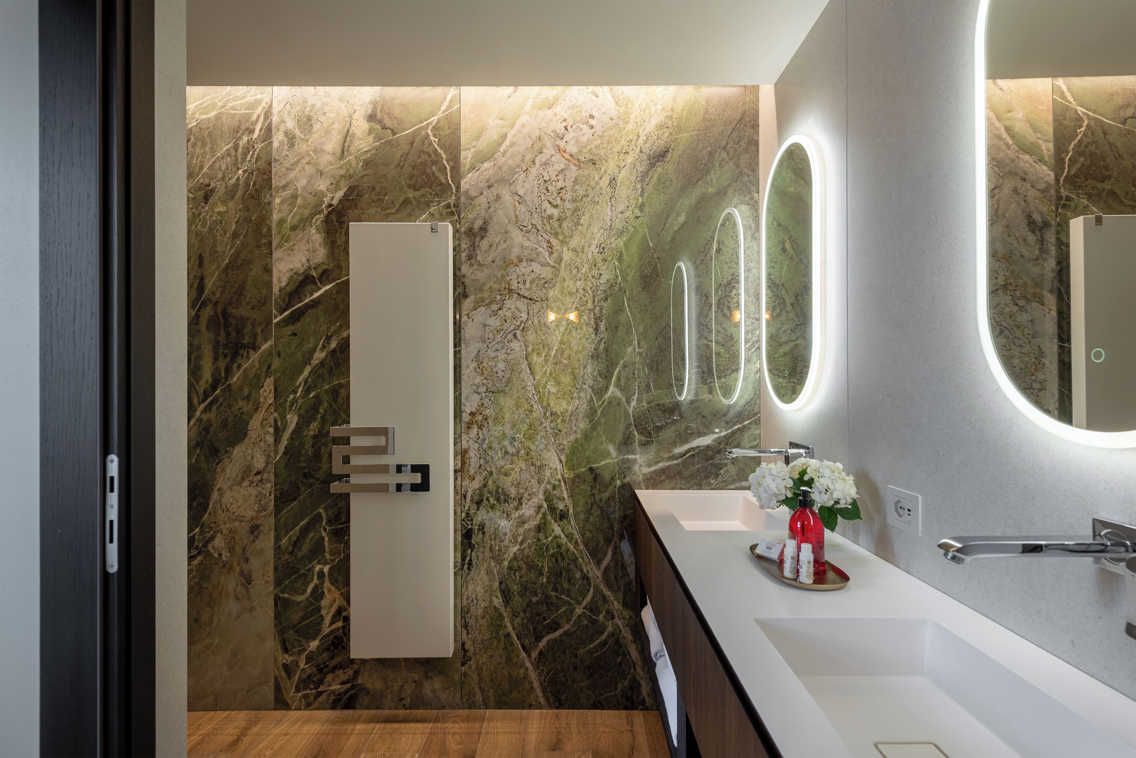 A modern bathroom with a marble wall, a large mirror, and a wooden vanity.