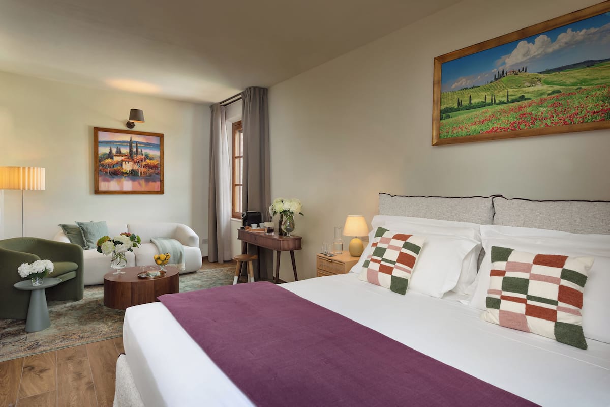 Een hotelkamer met een groot bed, een bureau, een stoel, een kleine tafel met bloemen en een schilderij aan de muur.