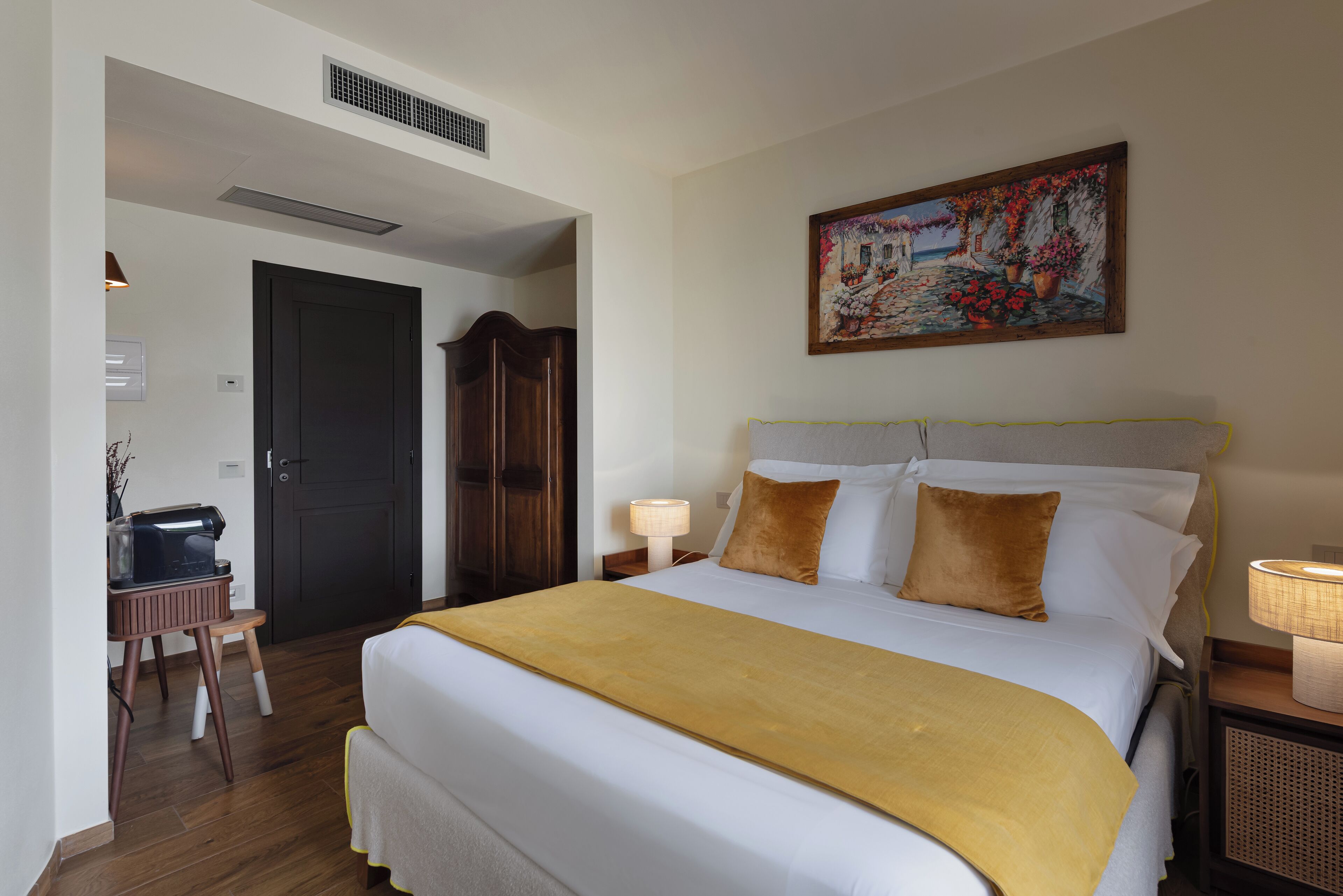 Un dormitorio ordenado con cama, lámparas de noche, un cuadro y un escritorio con cafetera.