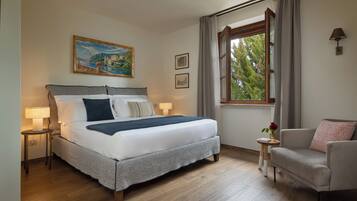 A neatly arranged bedroom with a large bed, bedside lamps, a small table with a vase, and a window with curtains.