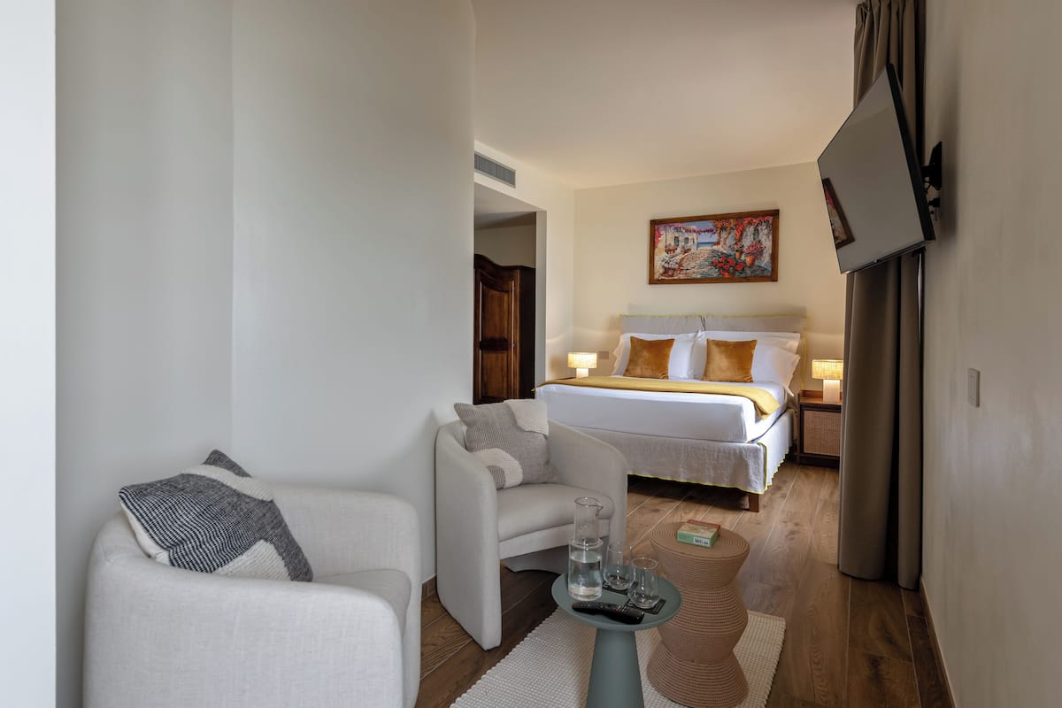 Een hotelkamer met een bed, een sofa, een televisie aan de muur en een schilderij boven het bed.