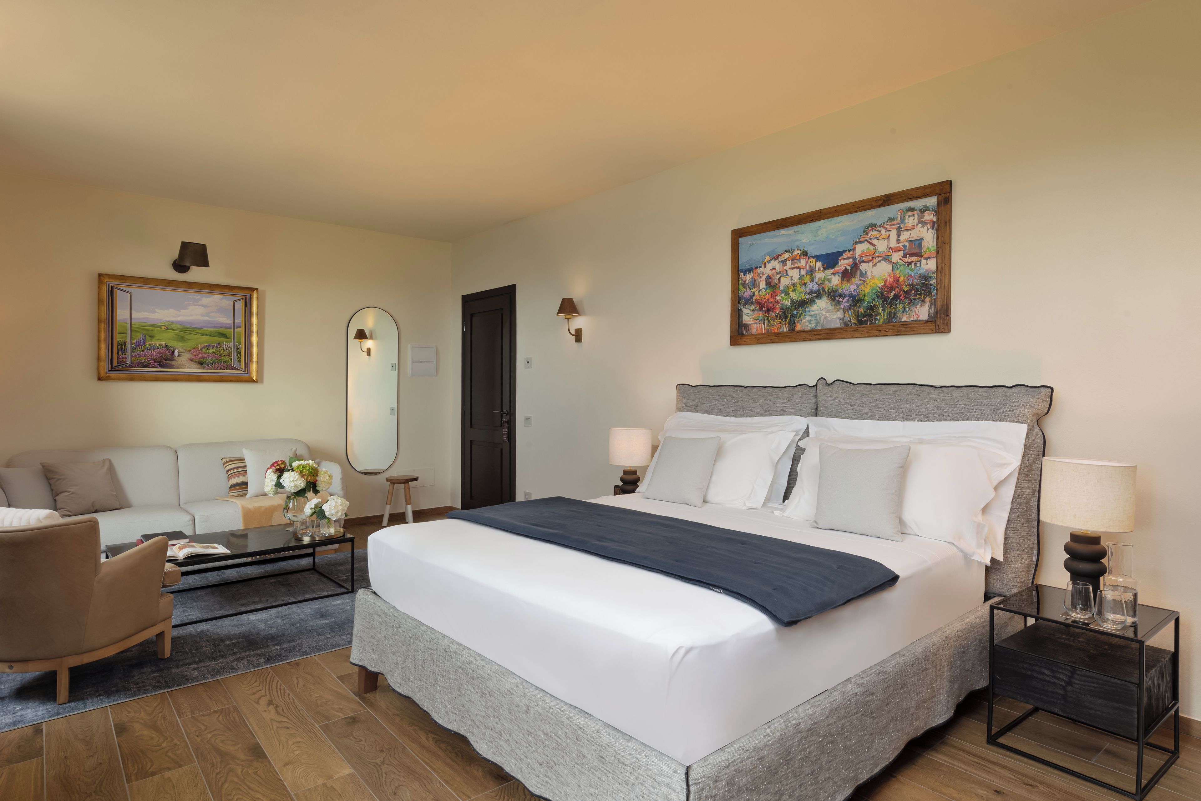 Habitación de hotel con cama, sofá, mesa de centro, mesita de noche con lámpara y un cuadro en la pared.