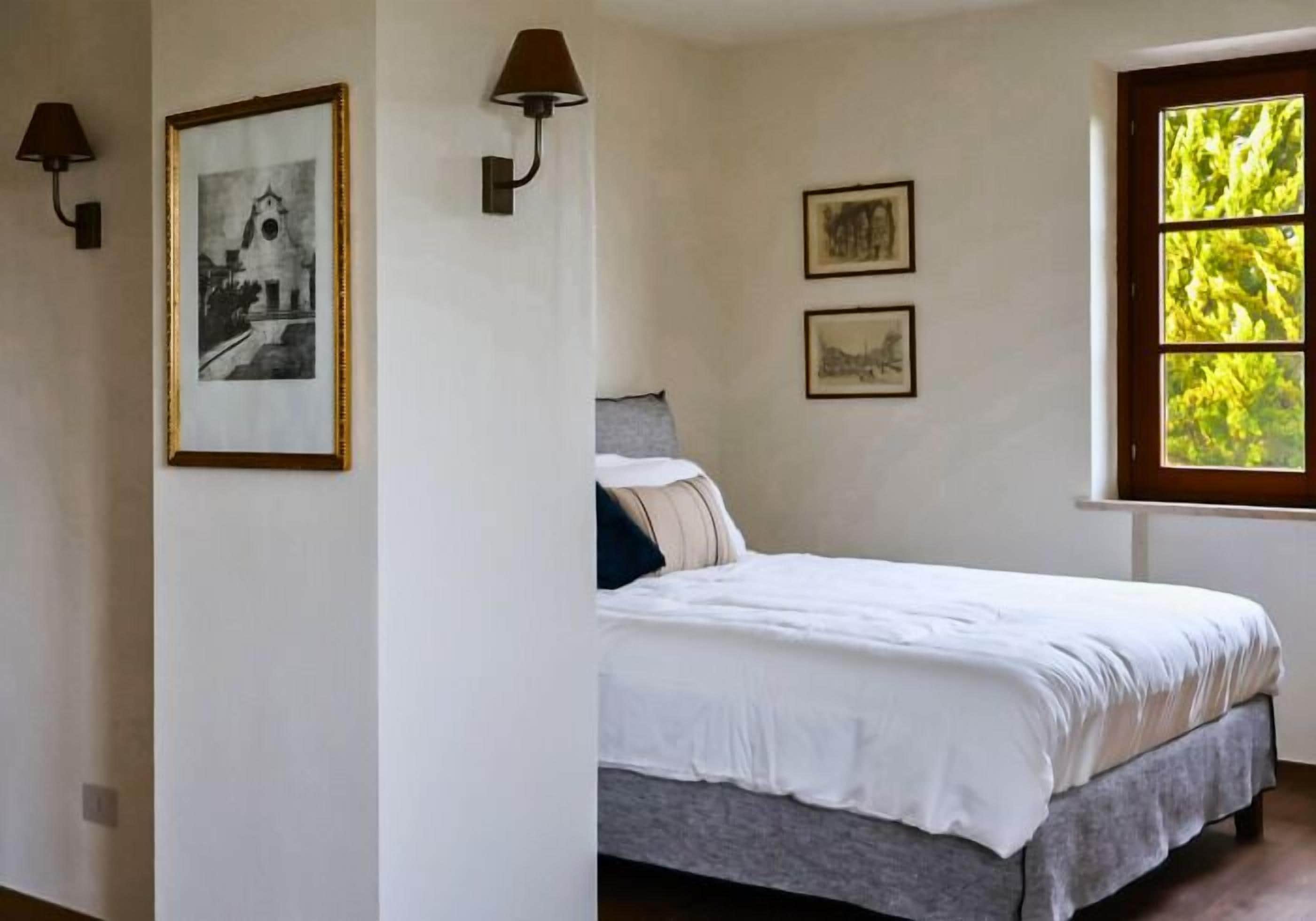 A bedroom with a bed, two wall-mounted lamps, and framed pictures on the wall.
