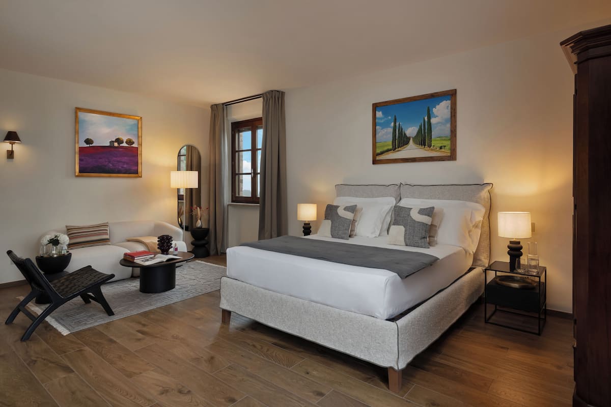Een moderne slaapkamer met een groot bed, nachtlampjes, een bank, een fauteuil en twee schilderijen aan de muur.