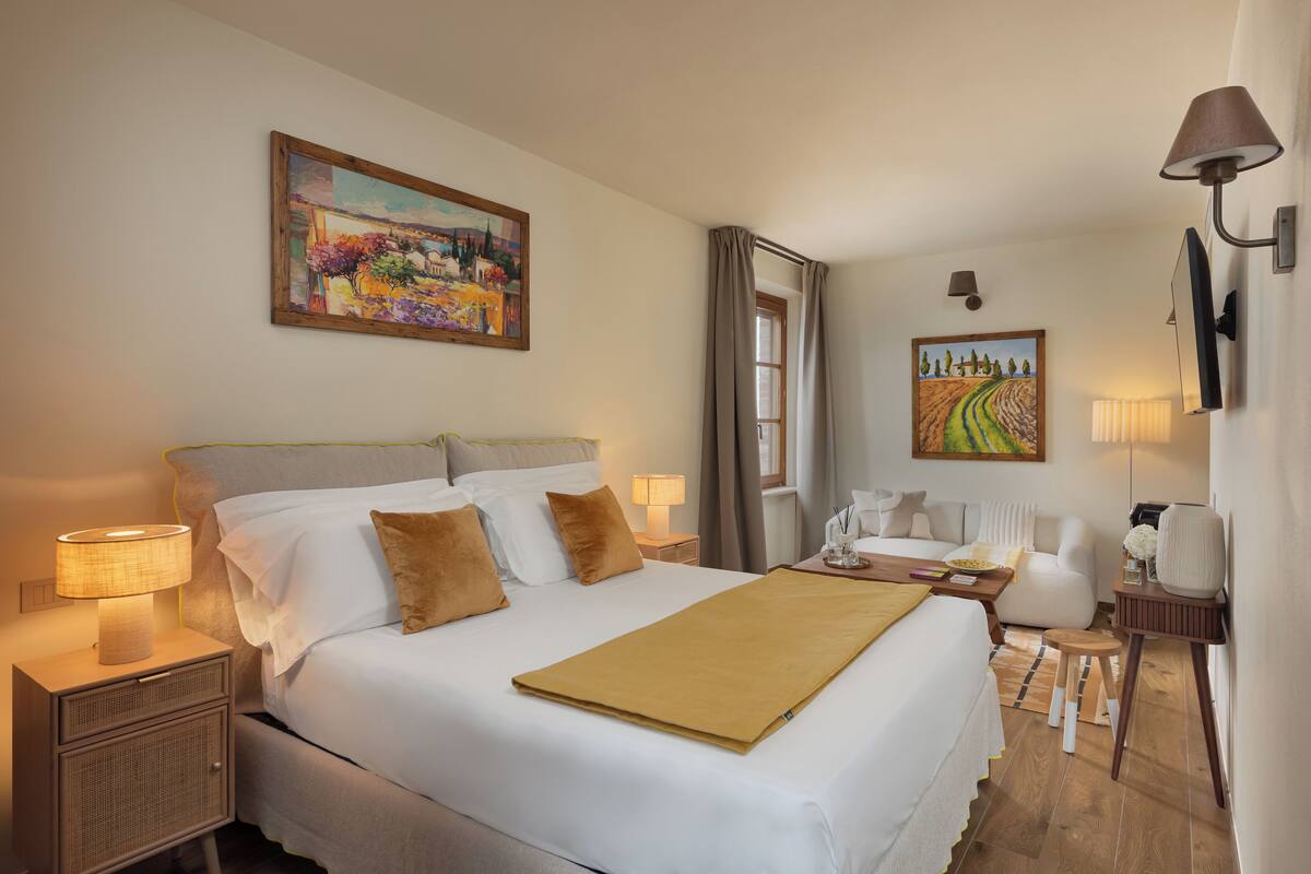 Een hotelkamer met een bed, nachtkastjes, lampen, een schilderij, een bureau en een stoel.