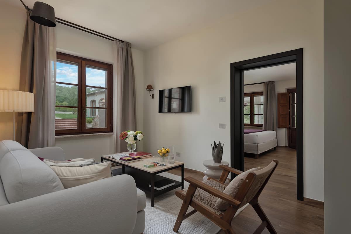 Een moderne woonkamer met een bank, een houten stoel, een salontafel en een aan de muur bevestigde televisie.