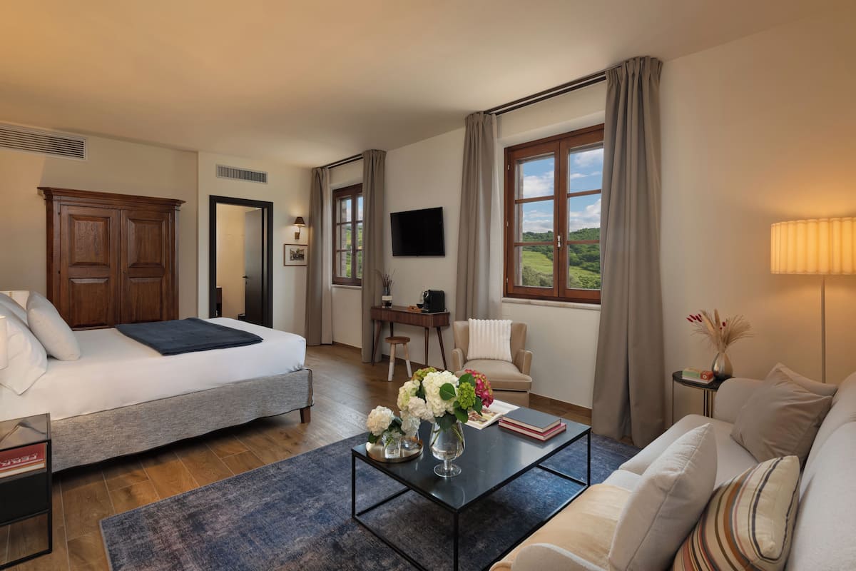 Hotelkamer met een bed, een slaapbank, een bijzettafeltje met bloemen, een televisie en uitzicht op groen.