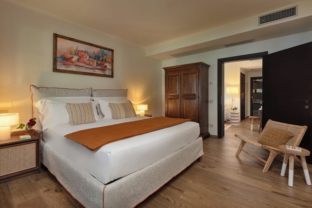 Een ruime slaapkamer met een groot bed, een houten garderobe en een stoel.