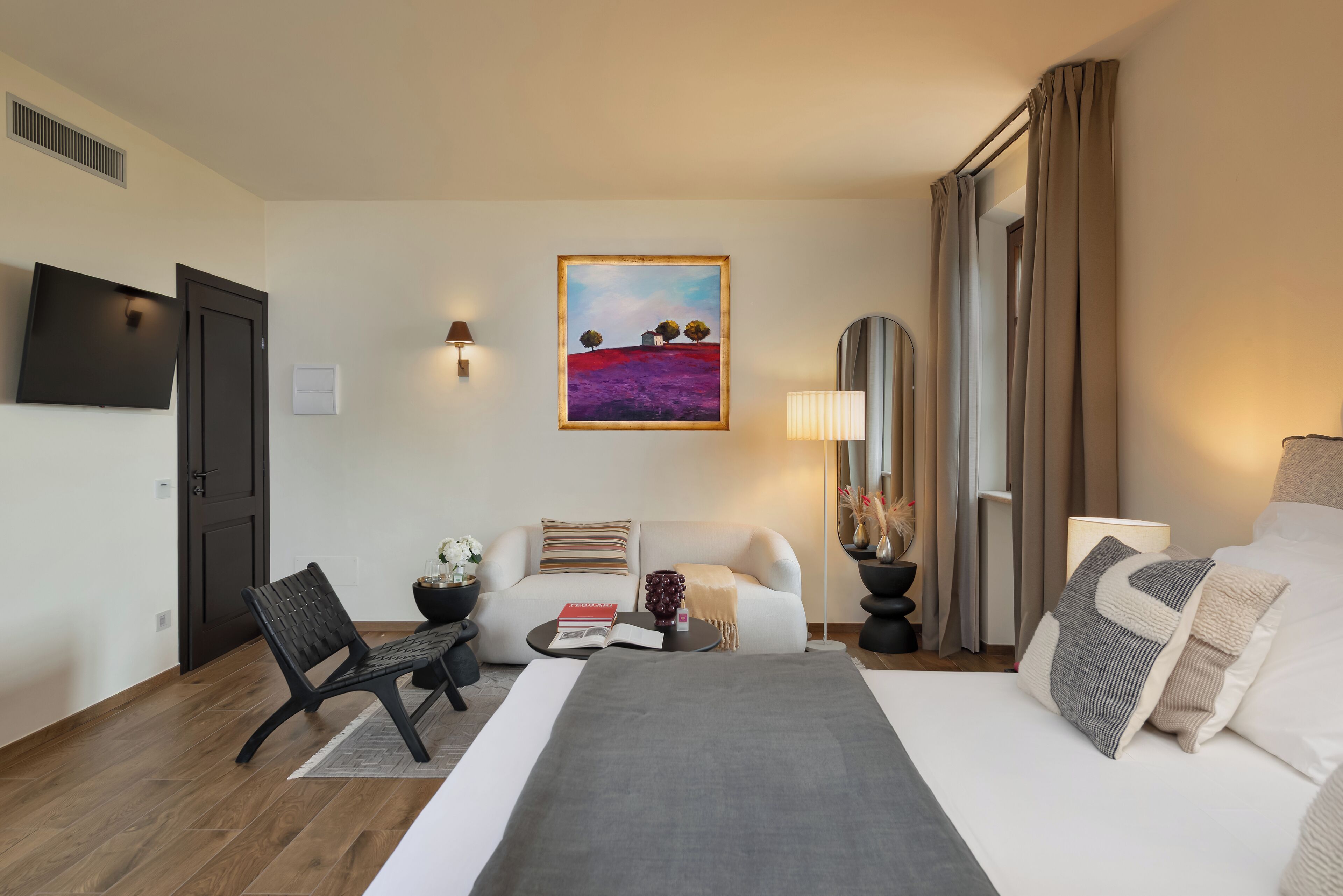 Una camera d'albergo con un letto, una poltrona, una sedia, un tavolino, un quadro e una televisione.