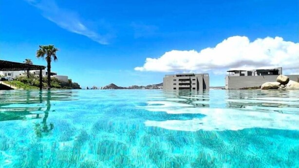 Una piscina azul cristalina con una palmera y edificios al fondo.