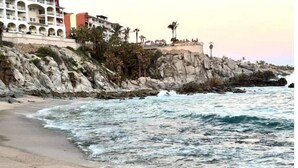 Un hotel frente al mar con varios balcones, un litoral rocoso y olas rompiendo en la playa.