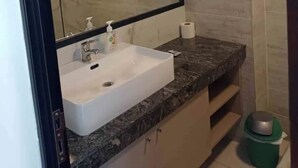 A modern bathroom with a large mirror, white sink, marble countertop, and a green trash bin. - Cozy central apartment, perfect for getaways (Salta)