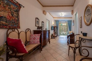 Quarto com um banco de madeira, uma escrivaninha, uma cadeira, tapeçaria e vista através de uma porta de vidro.