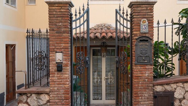 Una entrada protegida con un muro de piedra, una reja metálica y una puerta con paneles de vidrio.