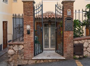 A gated entrance with a stone wall, a metal gate, and a door with glass panels. - (Casa d’arte Taormina) Alloggio con Patio+Parking (Taormina)