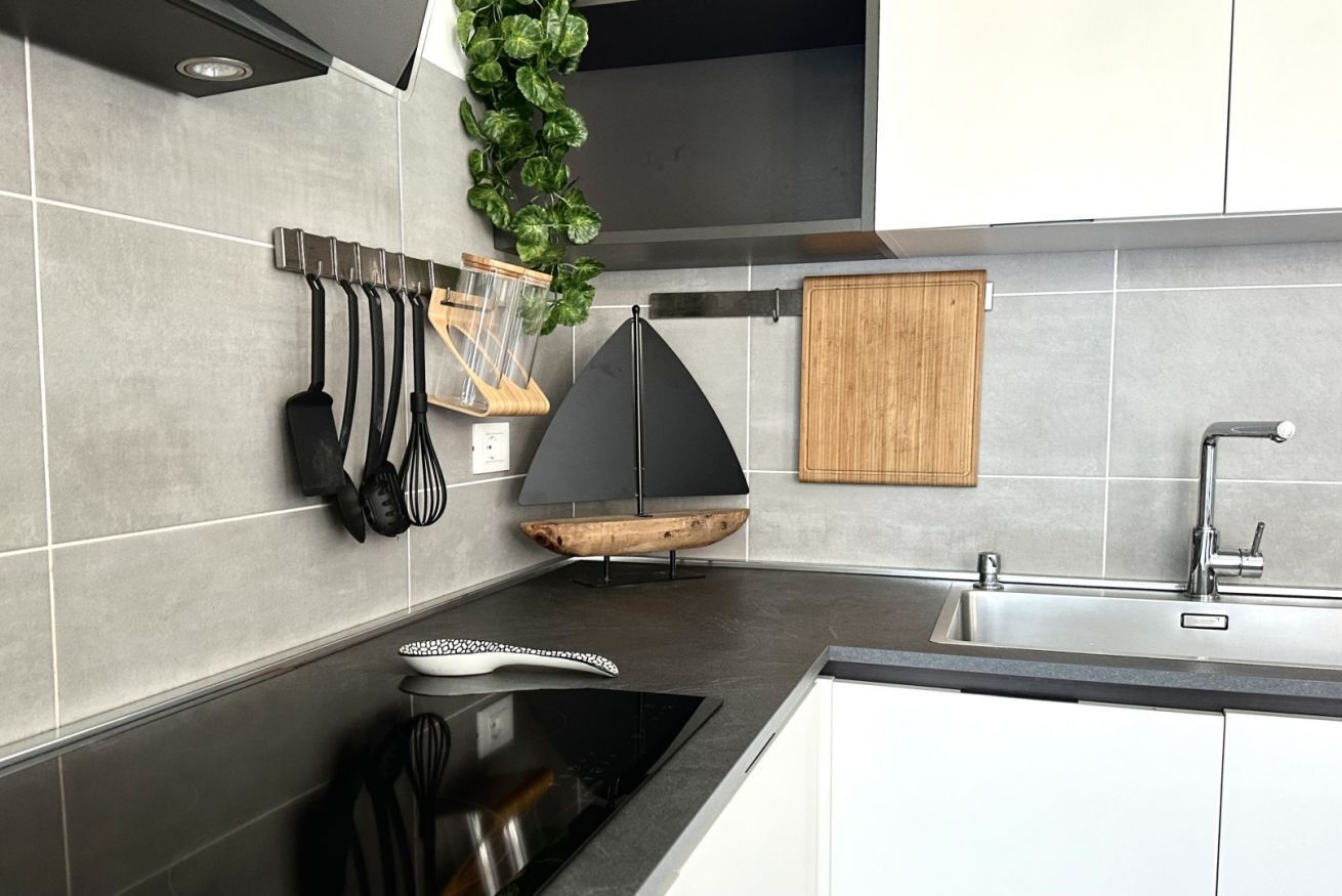 A modern kitchen with a black stove, a wooden cutting board, and a hanging utensil rack.